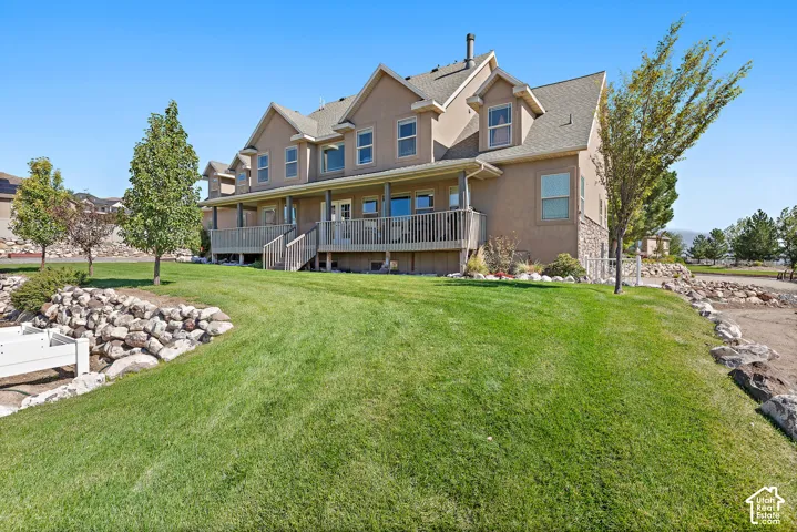 Expansive rear exterior featuring multiple dormer windows, a full-length wooden deck, and a stone retaining wall