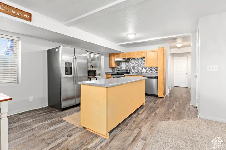 Kitchen featuring a central island with a stone-finish countertop, stainless steel appliances, wood cabinetry, and a patterned tile backsplash