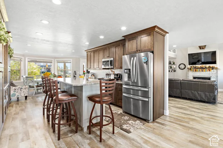 Kitchen featuring wood-finish flooring, stainless steel appliances, a center island with seating, recessed lighting, and a tile backsplash