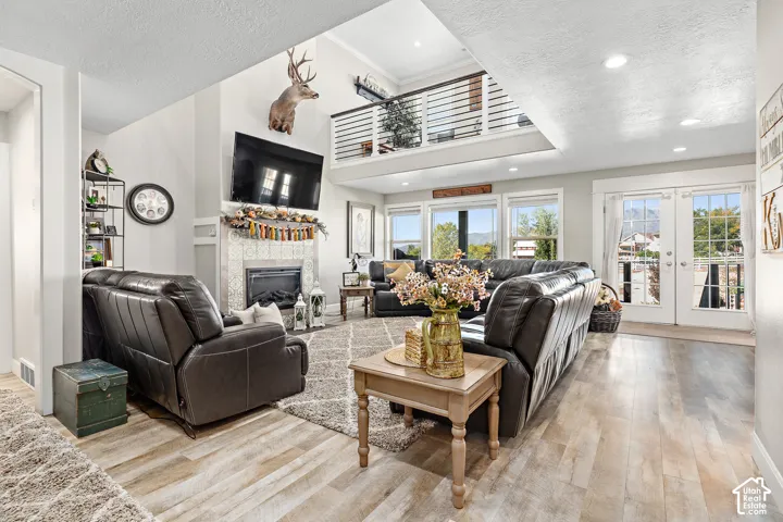 Vaulted ceiling, open mezzanine with metal railing, wood-finish flooring, fireplace with tile surround, and French doors