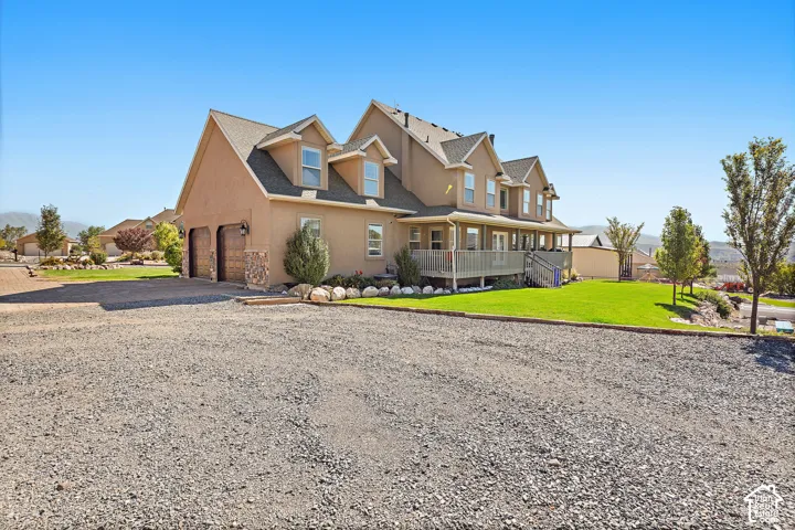 Stucco exterior residence with dormer windows, a covered porch, an attached garage with wood-paneled doors, and a manicured lawn