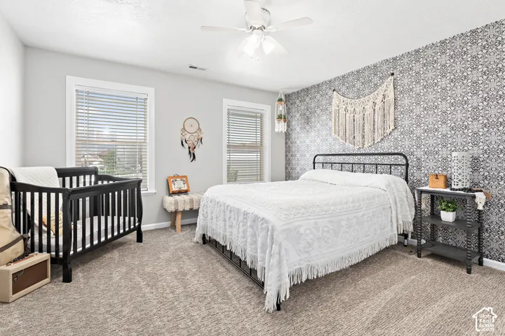 Textured carpet flooring, ceiling fan, multiple windows with blinds, accent wall with patterned wallpaper