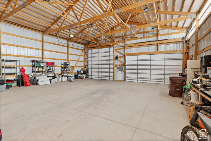 Spacious interior with exposed wood beam ceiling, concrete flooring, and multiple roll-up garage doors
