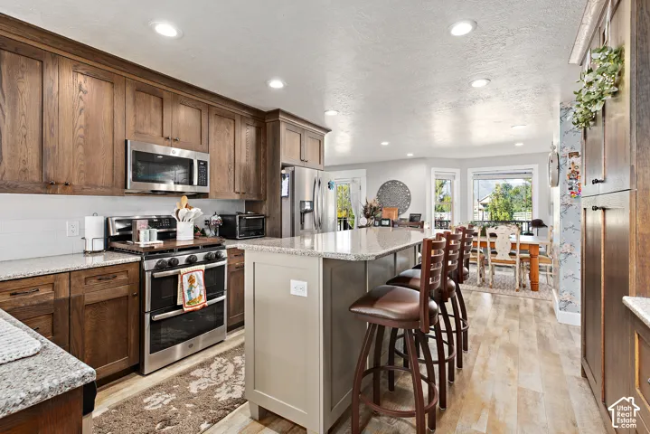 Gourmet kitchen with stainless steel appliances, wood-finish cabinetry, light-toned countertops, and an expansive island