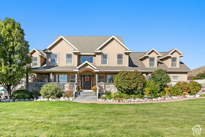 Expansive lawn with mature landscaping, a broad front porch with white railings, and a multi-level roofline