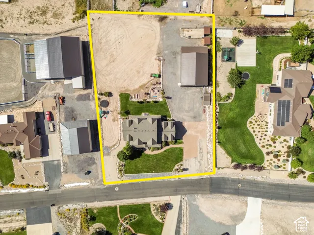 Aerial property overview featuring a main residence, two outbuildings, extensive unpaved areas, and established landscaping