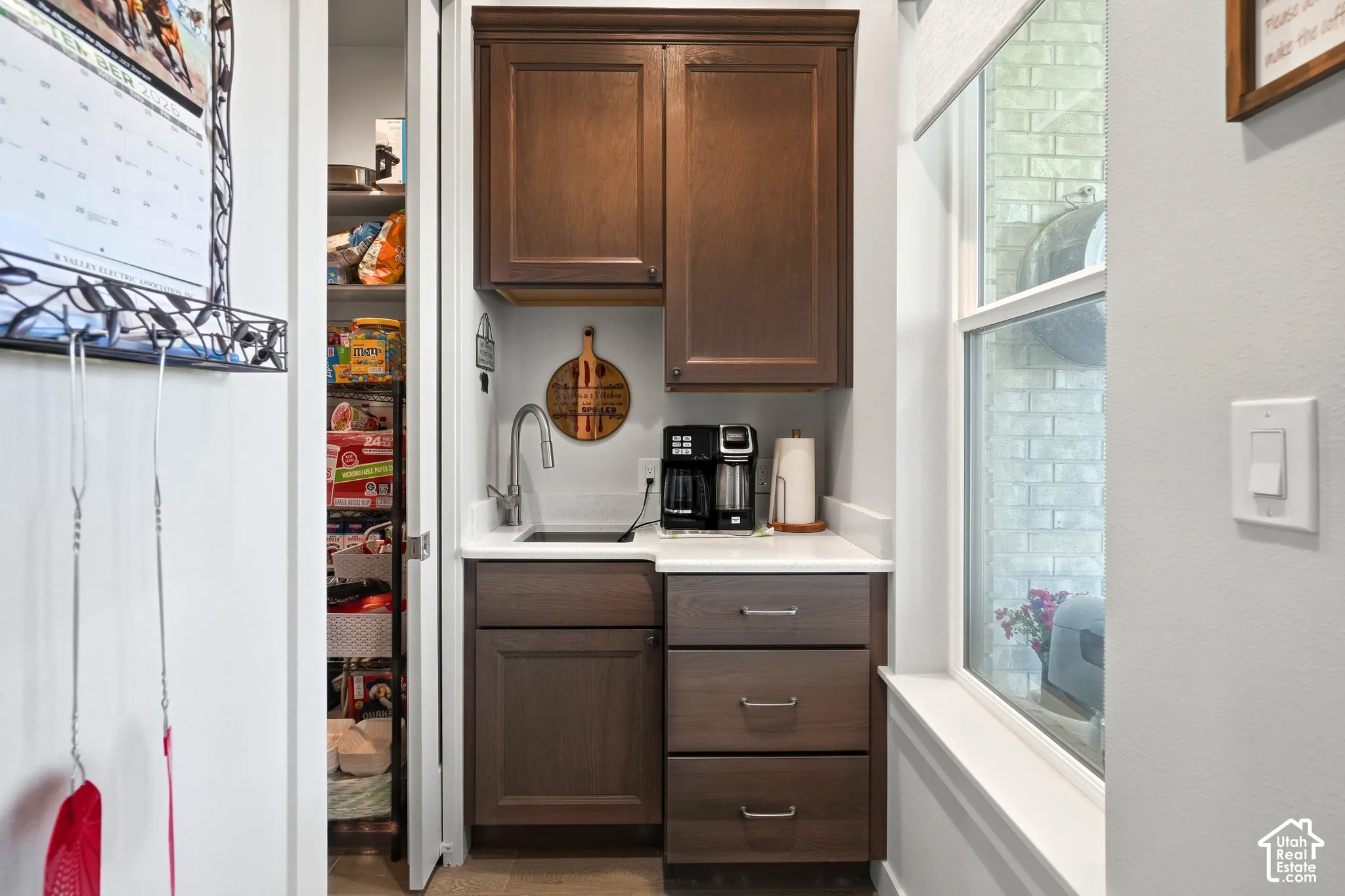 Wet bar with dark wood cabinetry, white countertop, and stainless steel sink