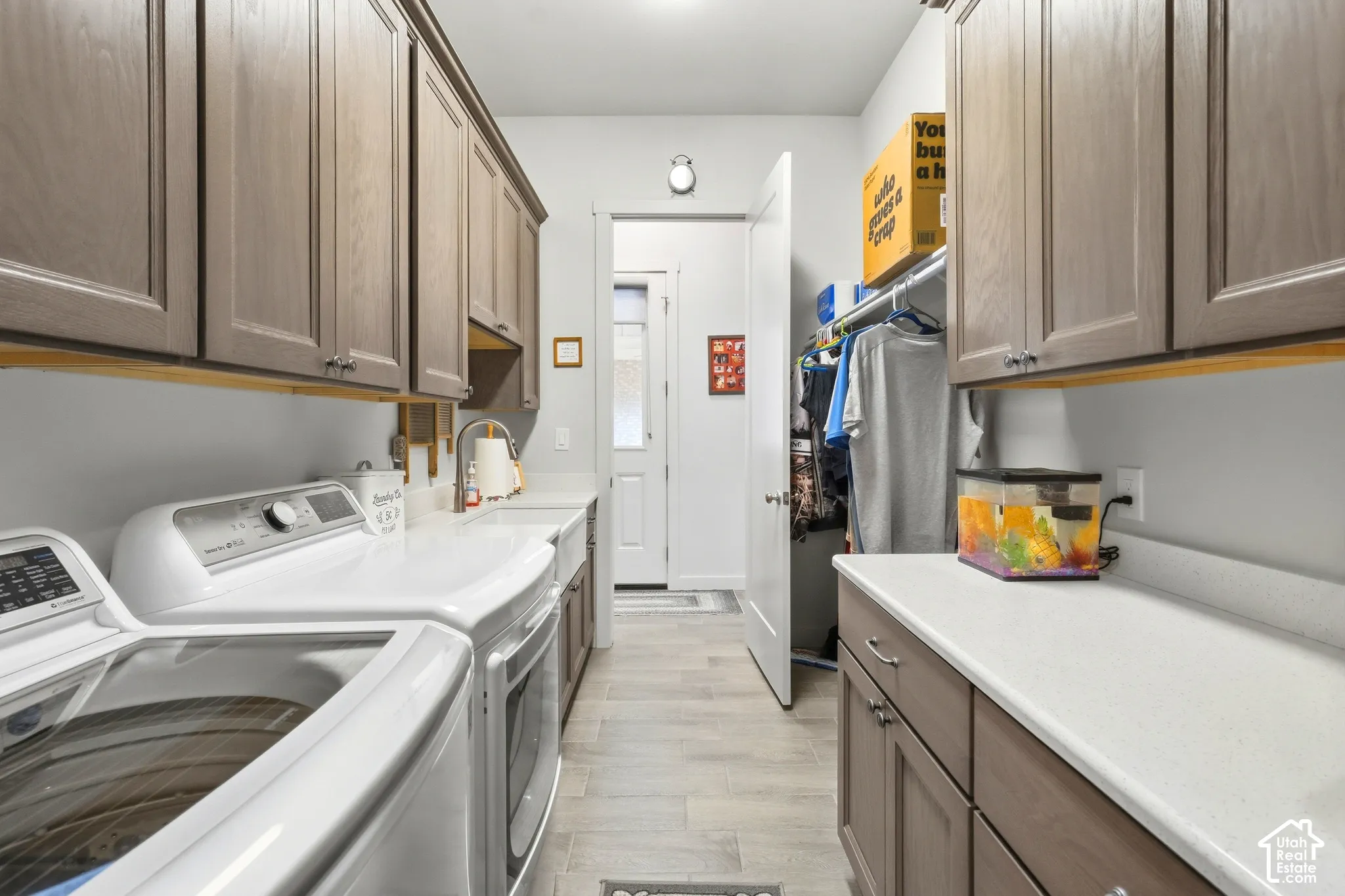 Laundry room featuring wood-finish flooring, shaker-style cabinetry, a built-in sink, and extensive countertop space