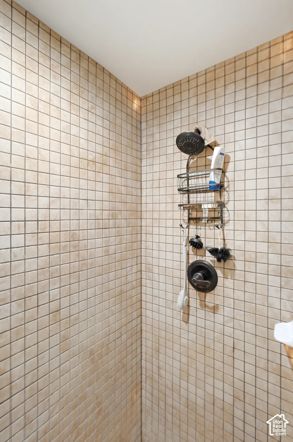 Shower enclosure with square tile surround and dark-finish shower head and controls