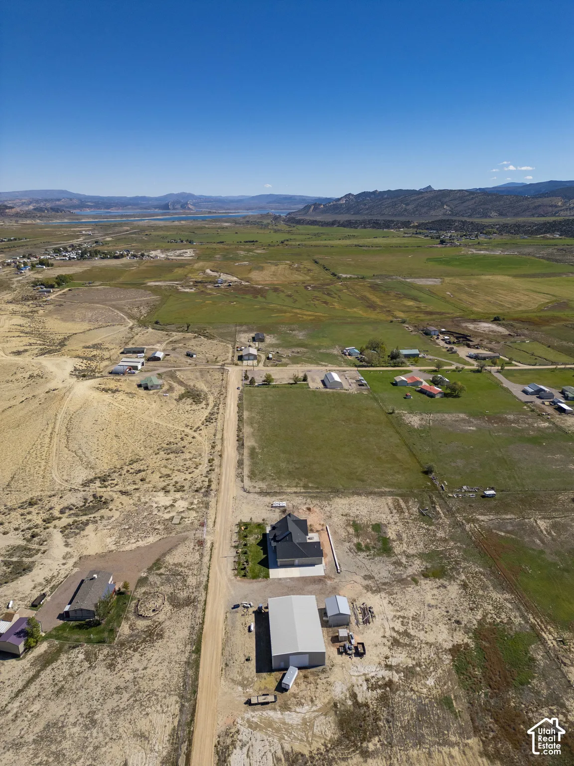 Expansive property featuring a modern residence, large outbuilding, and distant lake and mountain scenery
