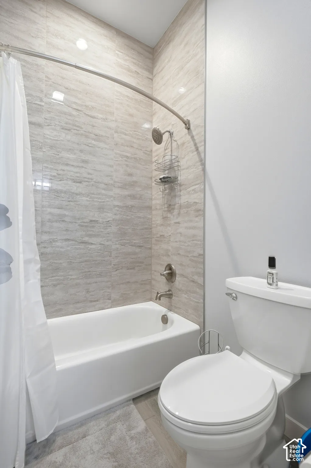 Bathtub and shower combination featuring neutral-toned tile surround, white porcelain fixtures, and brushed nickel hardware