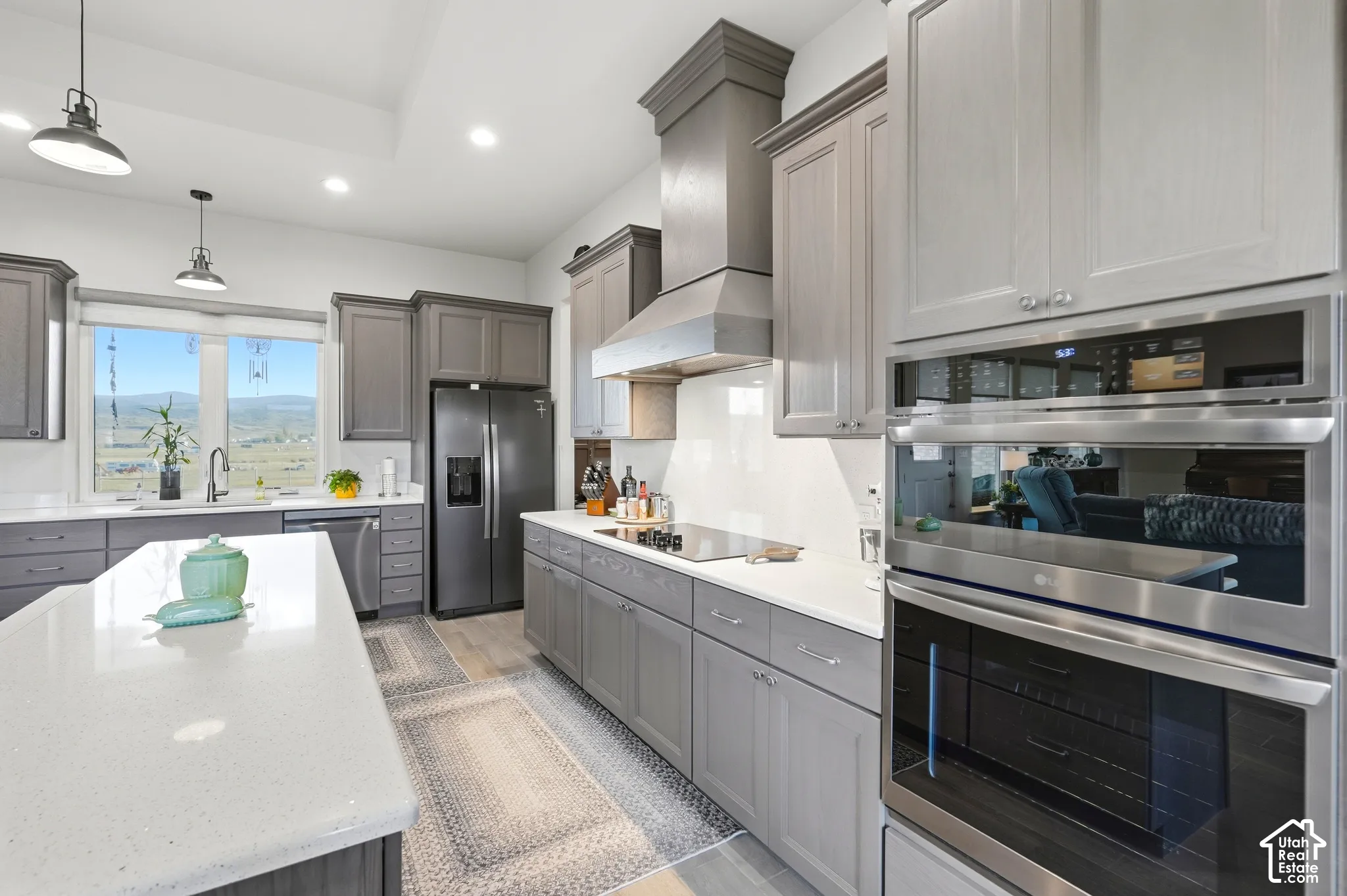 Kitchen featuring light gray cabinetry, white countertops, built-in stainless steel appliances, a black refrigerator, and pendant lighting