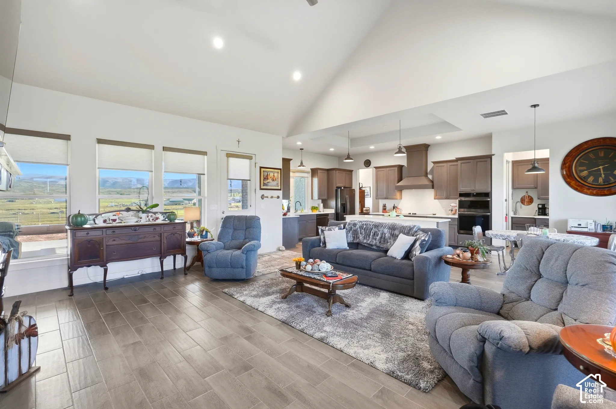 Spacious living area featuring vaulted ceilings, wood-finish tile flooring, recessed lighting, and a kitchen with dark wood cabinetry and a range hood