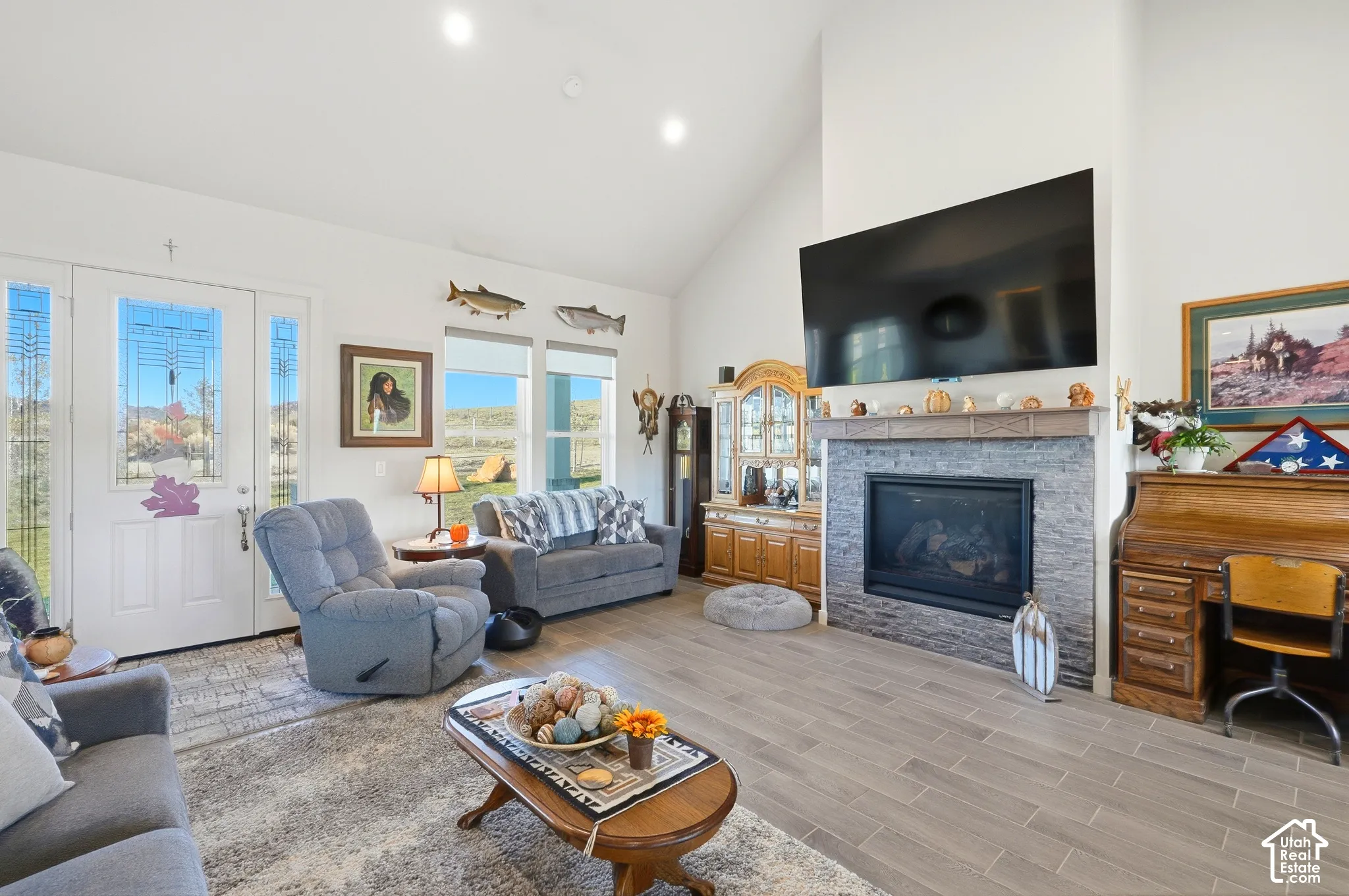 Vaulted ceiling, fireplace with stone surround and mantle, wood-finish flooring, recessed lighting, and large windows