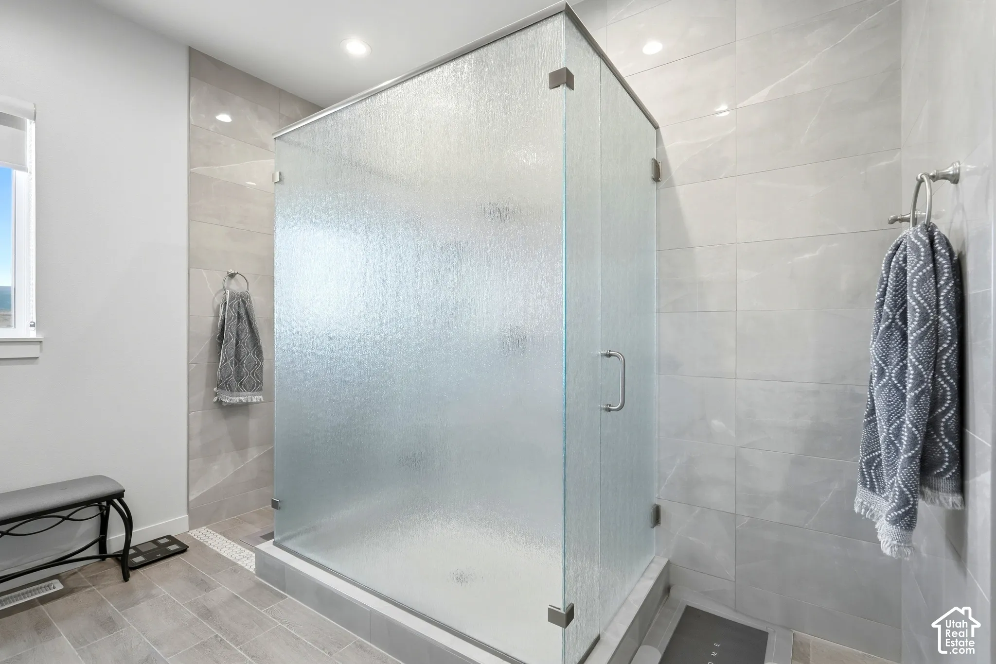 Glass-enclosed shower with textured glass panels, tiled shower surround, recessed lighting, and a window with a white frame