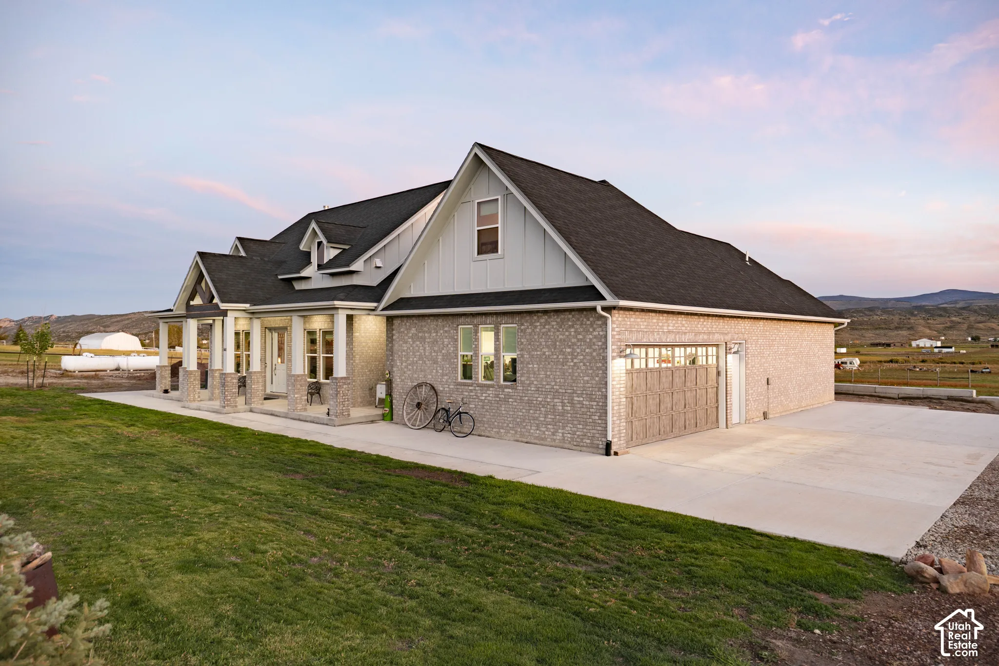 Brick and siding exterior with a dark shingle roof, featuring a covered front porch with columns, a two-car garage, and an expansive concrete driveway