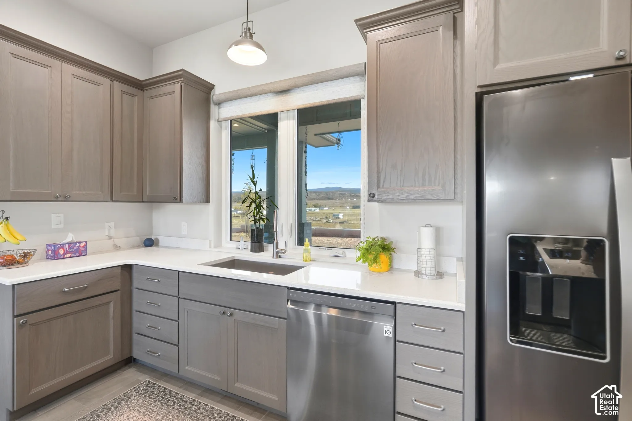 Gray cabinetry with crown molding, stainless steel appliances, undermount sink, white countertops, and a pendant light fixture