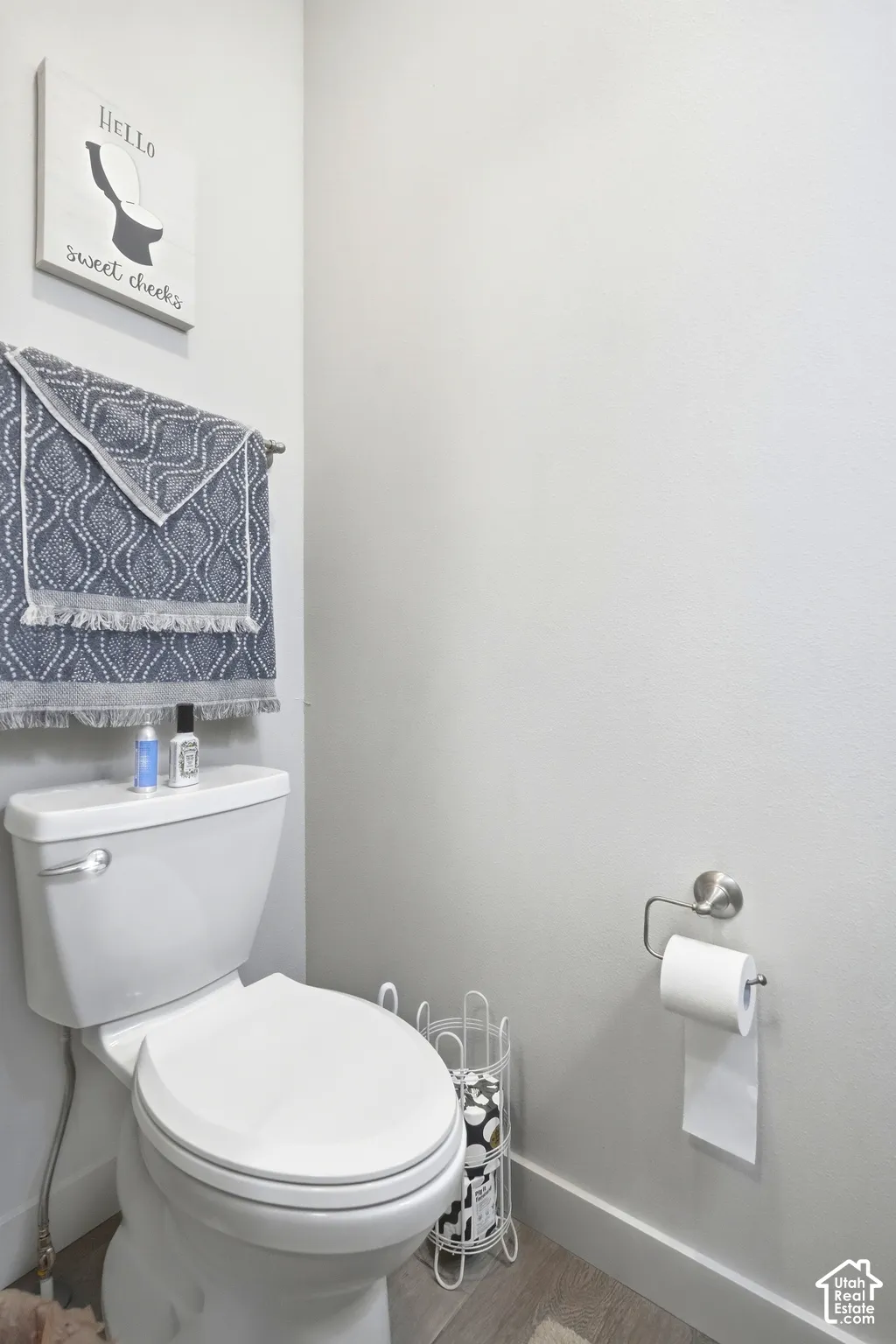 White toilet with a chrome flush lever, a wall-mounted towel bar, and wood-finish flooring