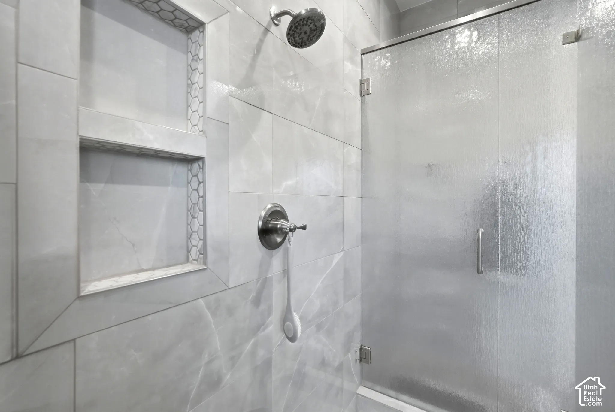 Shower with tiled walls, dual-shelf niche with hexagonal tile accents, brushed nickel showerhead, and a textured glass shower door