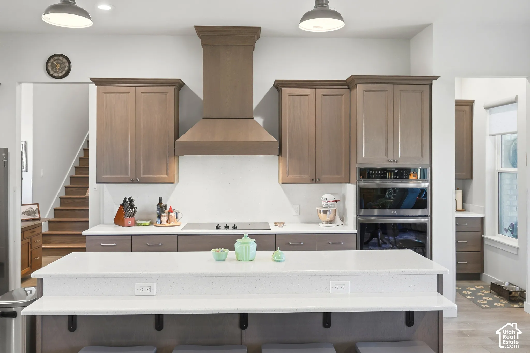 Modern kitchen featuring light wood-finish cabinetry, built-in stainless steel appliances, a center island with white countertop, and a built-in cooktop