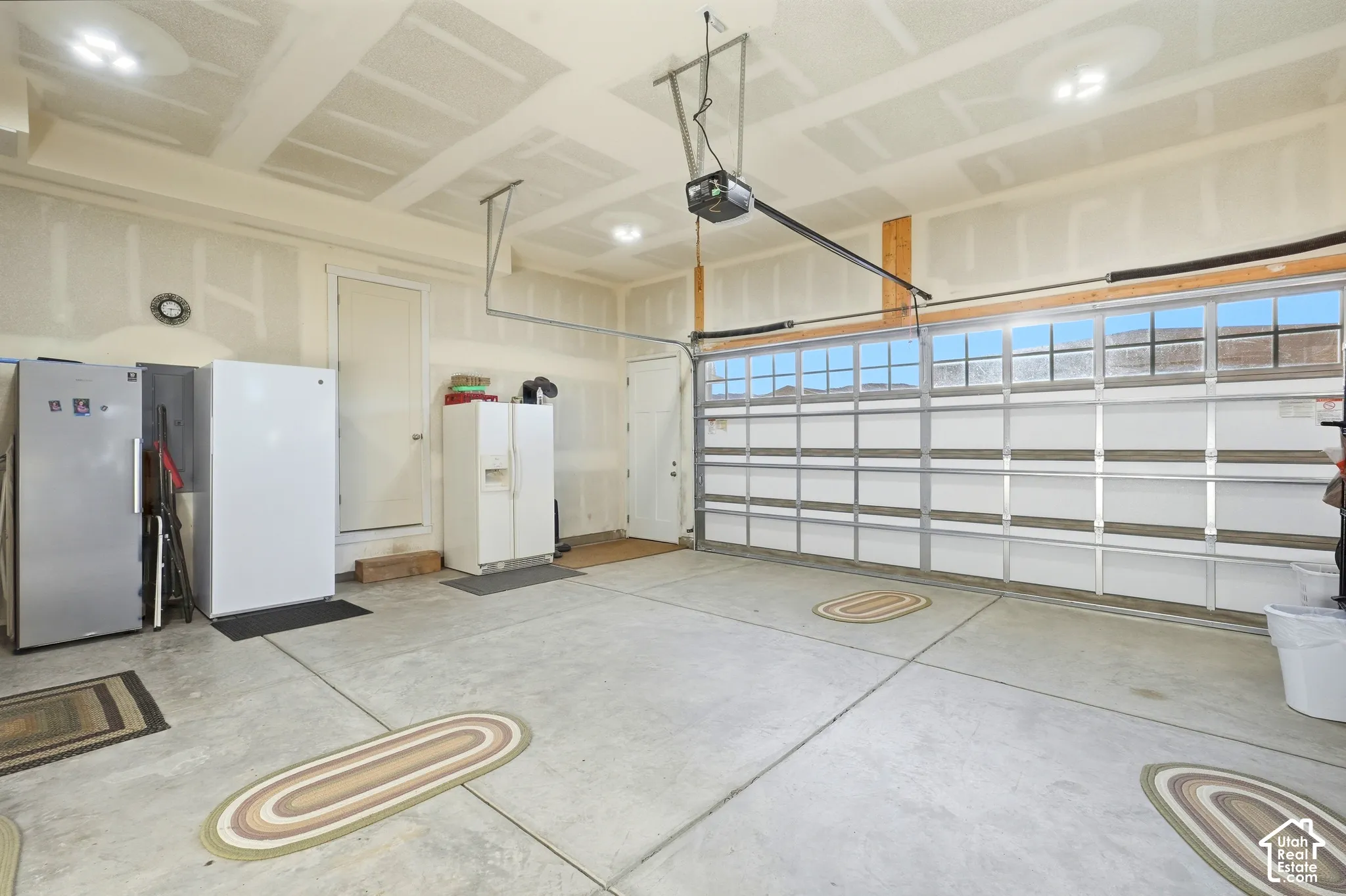 Concrete flooring with visible expansion joints, ceiling-mounted lighting, and a garage door with multiple transom window panes