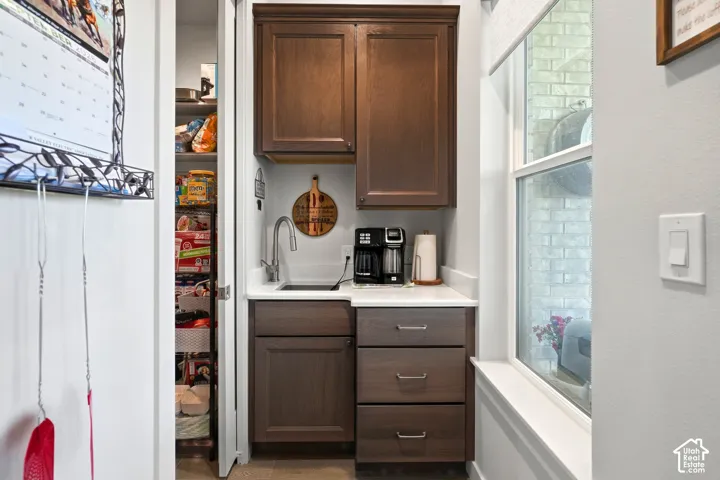 Wet bar with dark wood cabinetry, white countertop, and stainless steel sink
