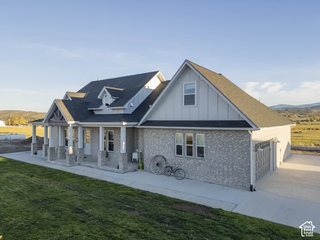 Exterior featuring light brick and vertical siding, a covered front porch with substantial columns, a two-car garage, and a concrete driveway