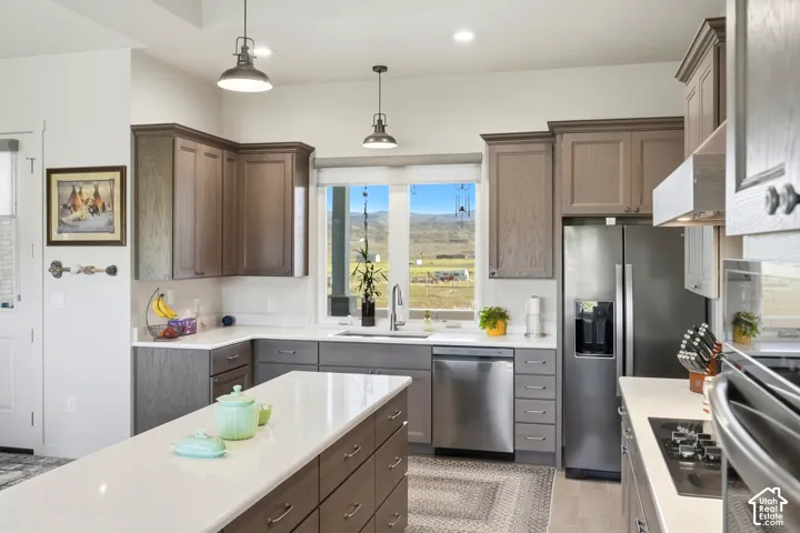 Kitchen featuring an island with a light-toned countertop, stainless steel appliances, upper and lower cabinetry, and recessed and pendant lighting
