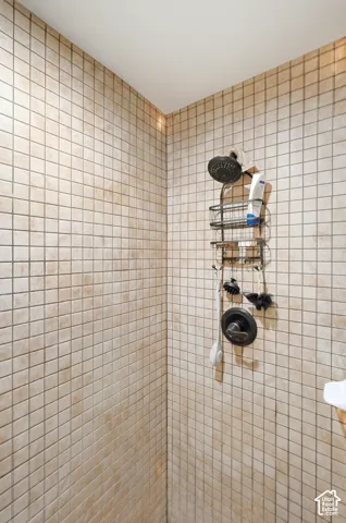 Shower enclosure with square tile surround and dark-finish shower head and controls
