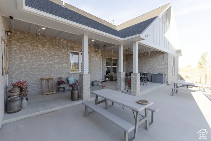 Expansive concrete patio featuring a covered porch, brick exterior, white columns, and white board-and-batten siding