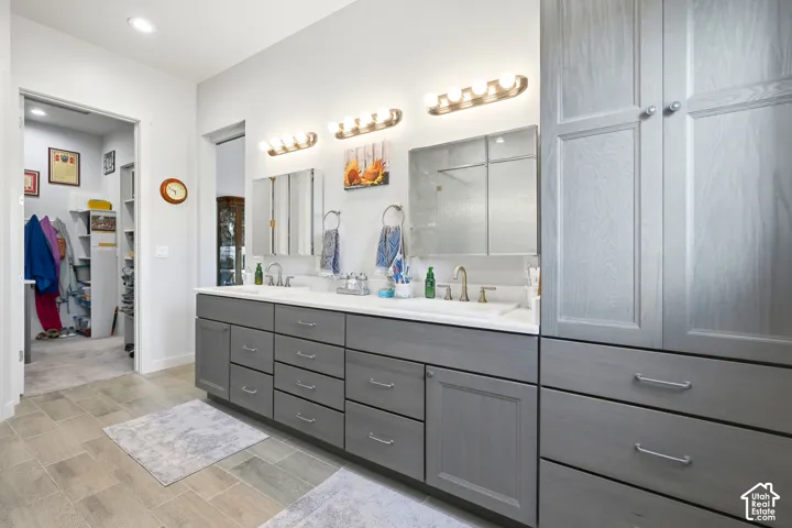 Dual sink vanity with grey cabinetry, white countertops, and a built-in linen cabinet