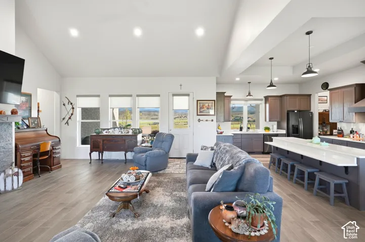 Open-concept living space featuring vaulted ceilings, wood-finish flooring, a kitchen with an extended island, recessed lighting, and ample natural light from multiple windows