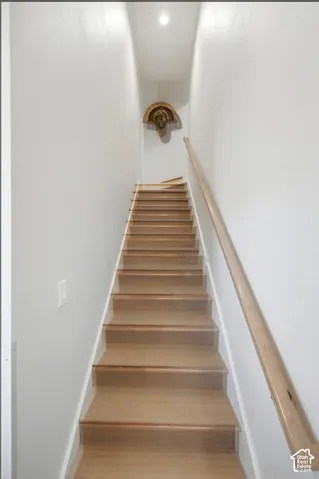 Hardwood staircase with a natural wood handrail, recessed ceiling lighting, and light-toned wall finishes