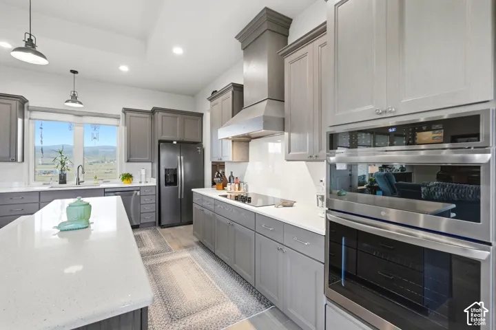 Kitchen featuring light gray cabinetry, white countertops, built-in stainless steel appliances, a black refrigerator, and pendant lighting