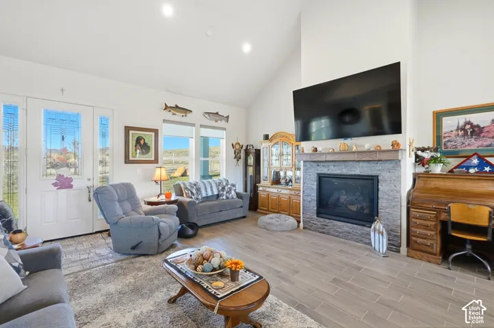 Vaulted ceiling, fireplace with stone surround and mantle, wood-finish flooring, recessed lighting, and large windows