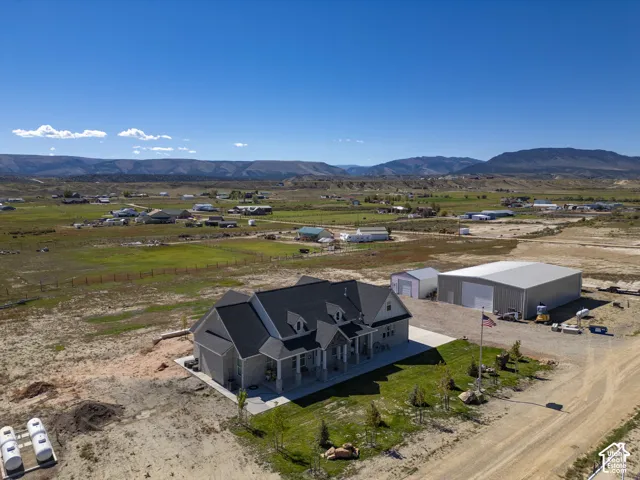 Expansive property featuring a single-story residence with a covered porch, a large detached garage, a secondary outbuilding, and mountain scenery