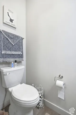 White toilet with a chrome flush lever, a wall-mounted towel bar, and wood-finish flooring