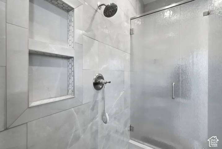 Shower with tiled walls, dual-shelf niche with hexagonal tile accents, brushed nickel showerhead, and a textured glass shower door