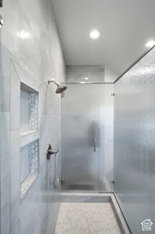 Walk-in shower with full-height tile surround, built-in recessed shelving, rainfall showerhead, and a frameless textured glass door