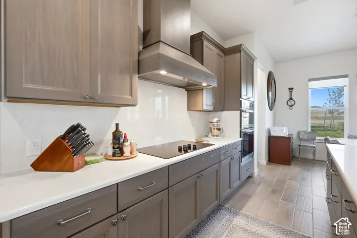 Kitchen featuring wood-finish cabinetry, quartz countertops, a built-in cooktop, a stainless steel range hood, and wood-finish flooring