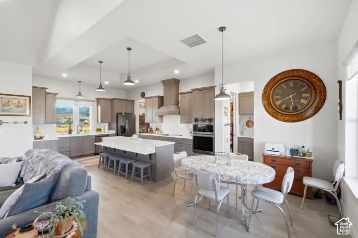 Open-concept living space featuring a kitchen with gray cabinetry, a large island with seating, pendant lighting, and wood-finish flooring