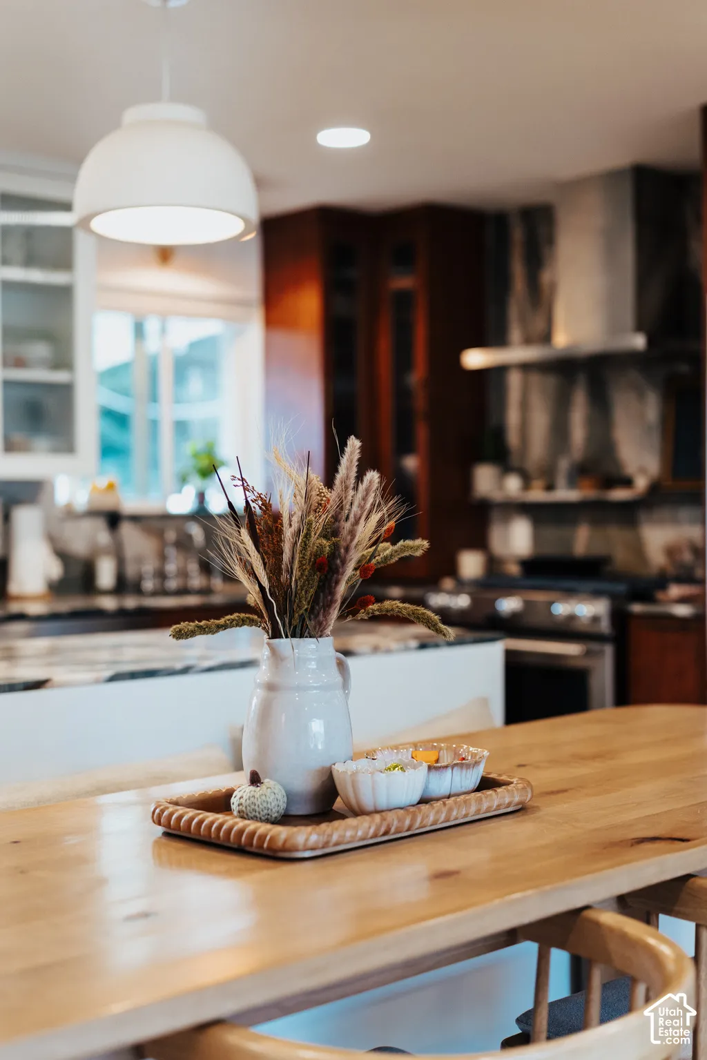 Kitchen featuring custom dark-toned cabinetry, high-contrast countertop with a prominent island, professional-grade range with a stainless steel vent hood, and a pendant light fixture