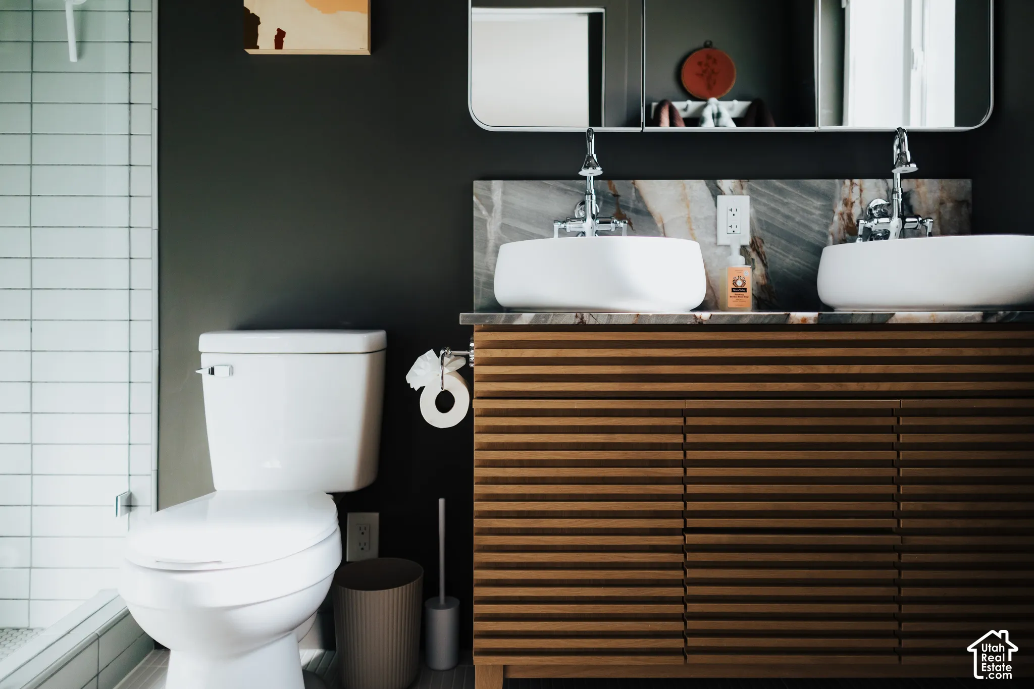 Slatted wood vanity featuring dual vessel sinks, stone backsplash, and wall-mounted faucets, accented by a rectangular mirror