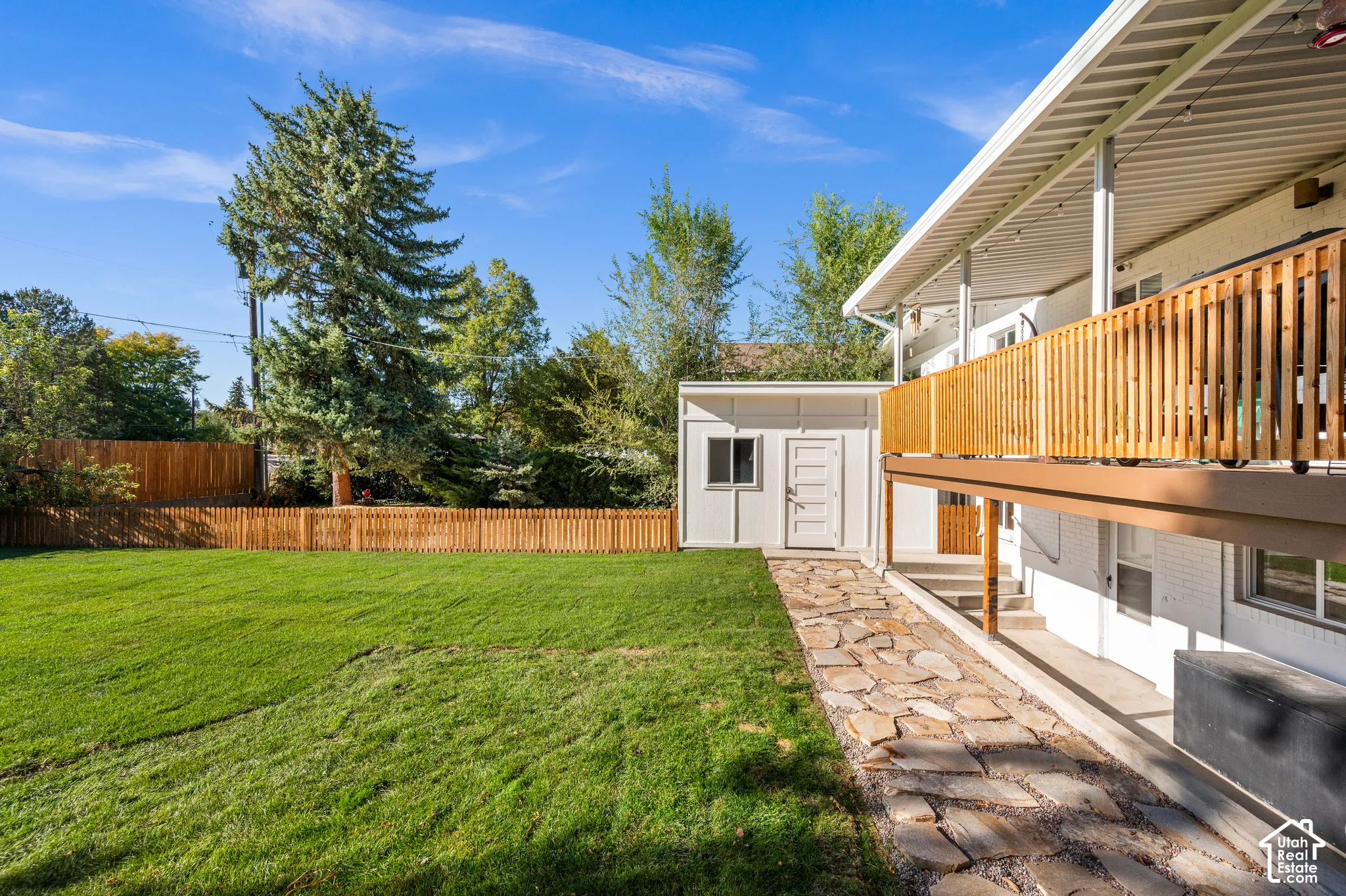Expansive backyard featuring a manicured lawn, full privacy fencing, a stone pathway, and a detached shed