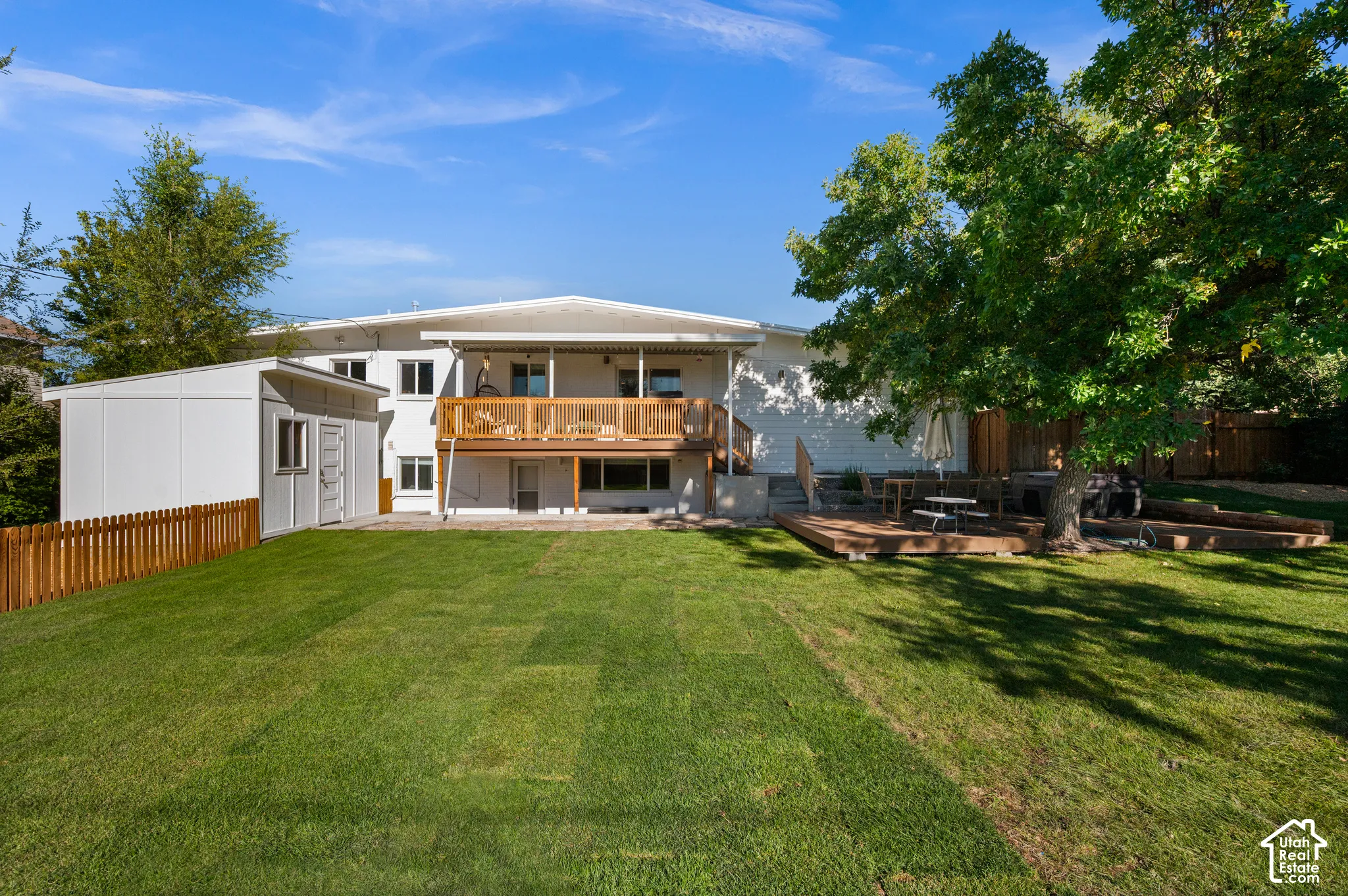 Expansive backyard featuring a large elevated wood deck, a ground-level wood patio, a mature tree, and a detached storage shed