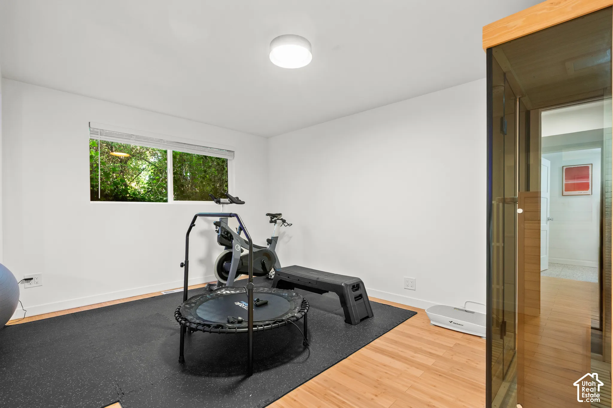 Room featuring wood-finish flooring, a window with outdoor scenery, and a built-in sauna with a glass door