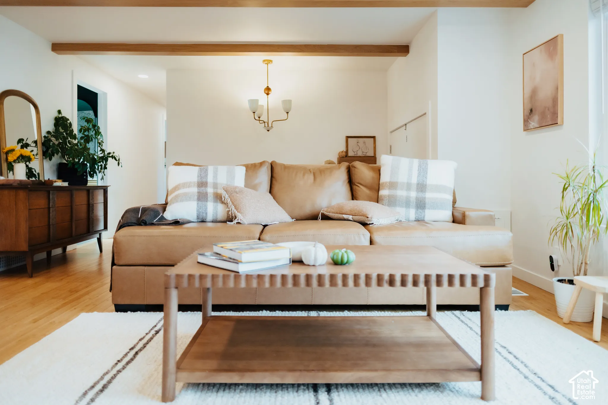 Exposed wood ceiling beams, wood-finish flooring, and a multi-arm brass chandelier