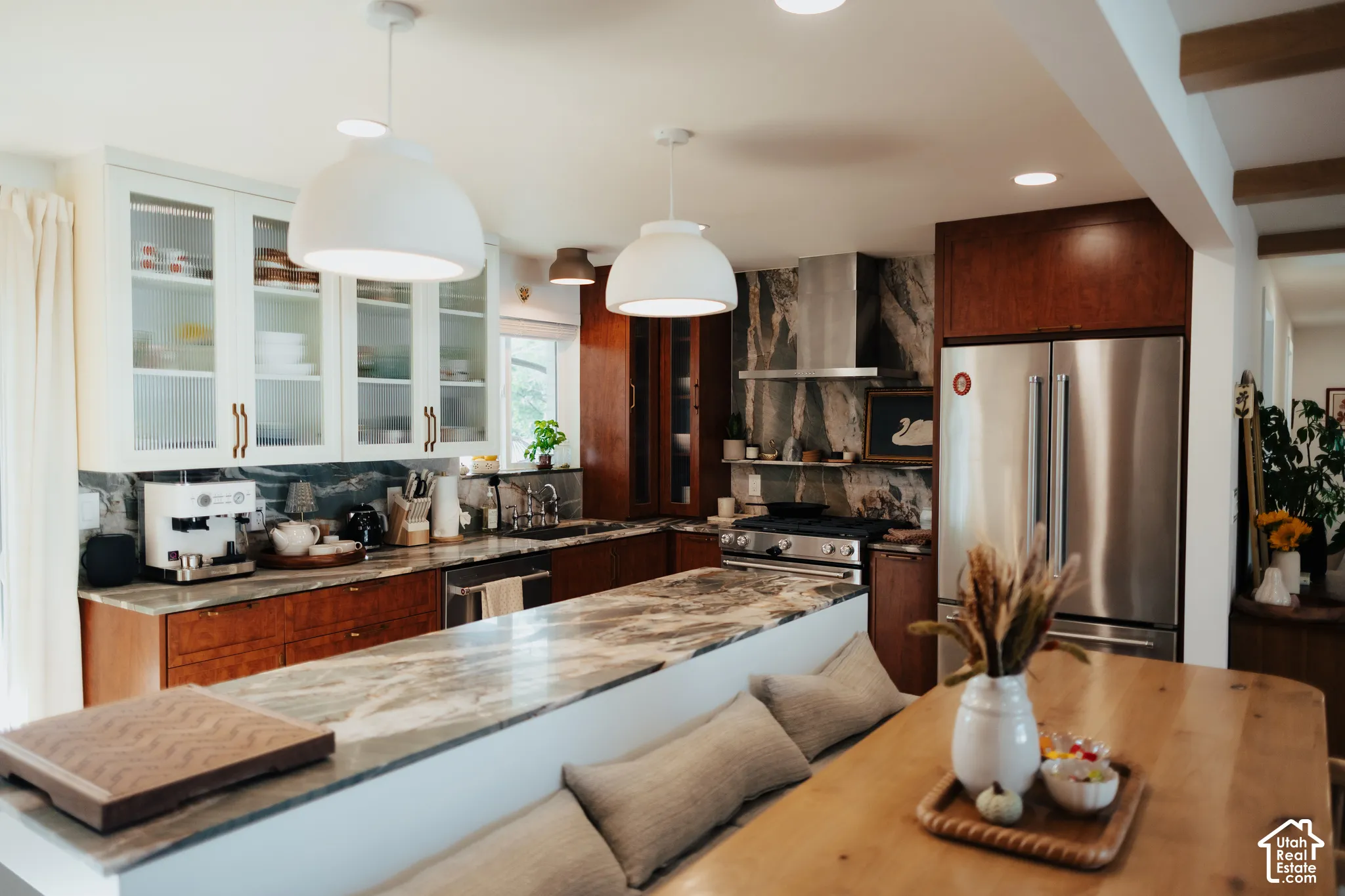 Kitchen featuring stone countertops, custom cabinetry with glass-front uppers, stainless steel professional-grade range, full-height stone backsplash, and dual pendant lighting