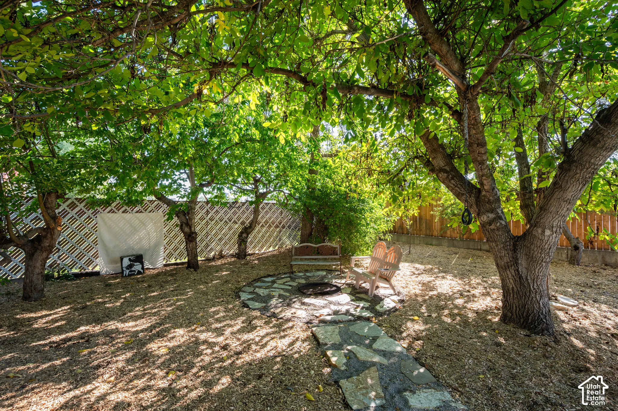 Backyard area featuring established trees, a stone pathway, a gravel ground covering, and a lattice fence