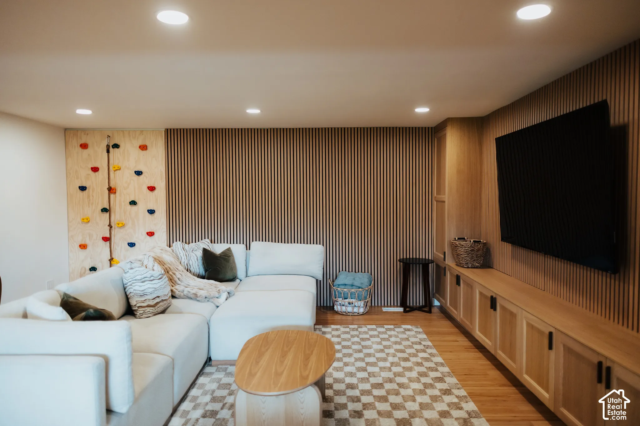 Custom climbing wall with integrated handholds, vertical wood slat accent wall, built-in light wood cabinetry, and recessed lighting